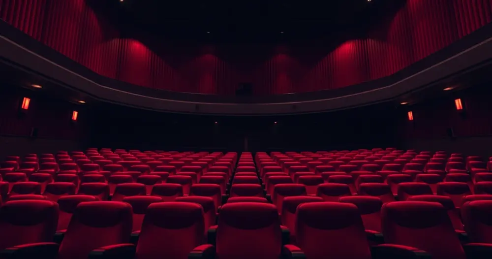 Sala de cinema vazia, com poltronas vermelhas e luz baixa